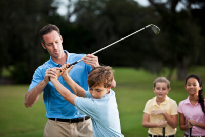 A golf instructor adjusting the boy's grip on the golf club